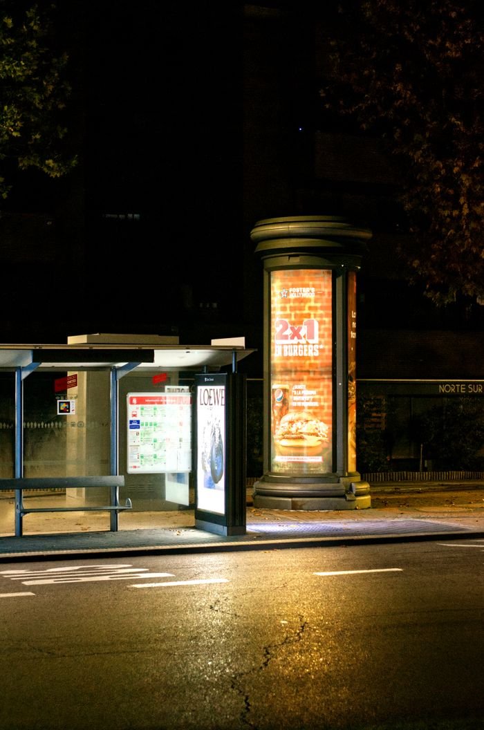 A well-lit urban bus stop at night with illuminated advertisements on the city street.
