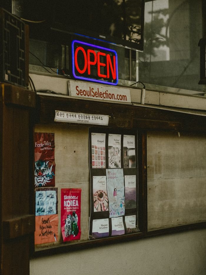 A city storefront featuring a vibrant neon 'Open' sign with various posters in Seoul.