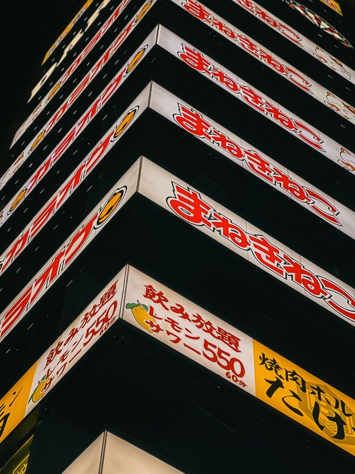 contact-hero Vibrant neon signs on a night-time urban building create a lively city scene.